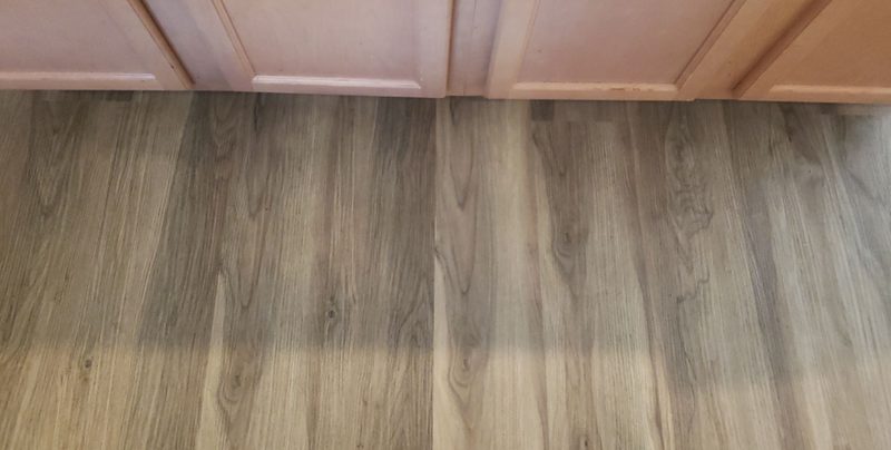 New grey-brown luxury vinyl plank floor meeting kitchen cabinets