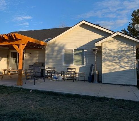 Back of a tan house with a wood pergola before repainting